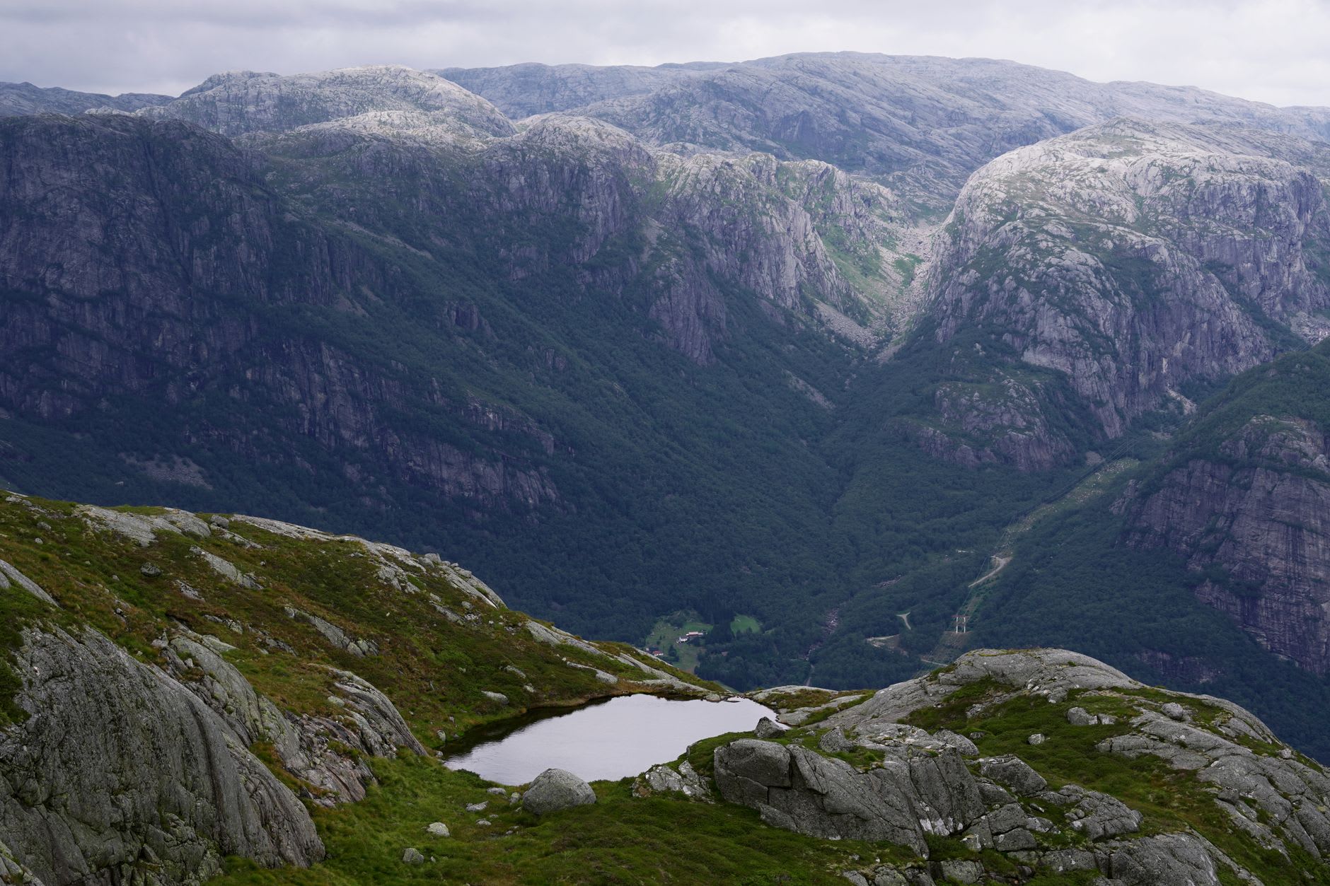 A lone hiker stepping onto the Kjeragbolten boulder wedged in the chasm with the Lysefjord a thousand metres below