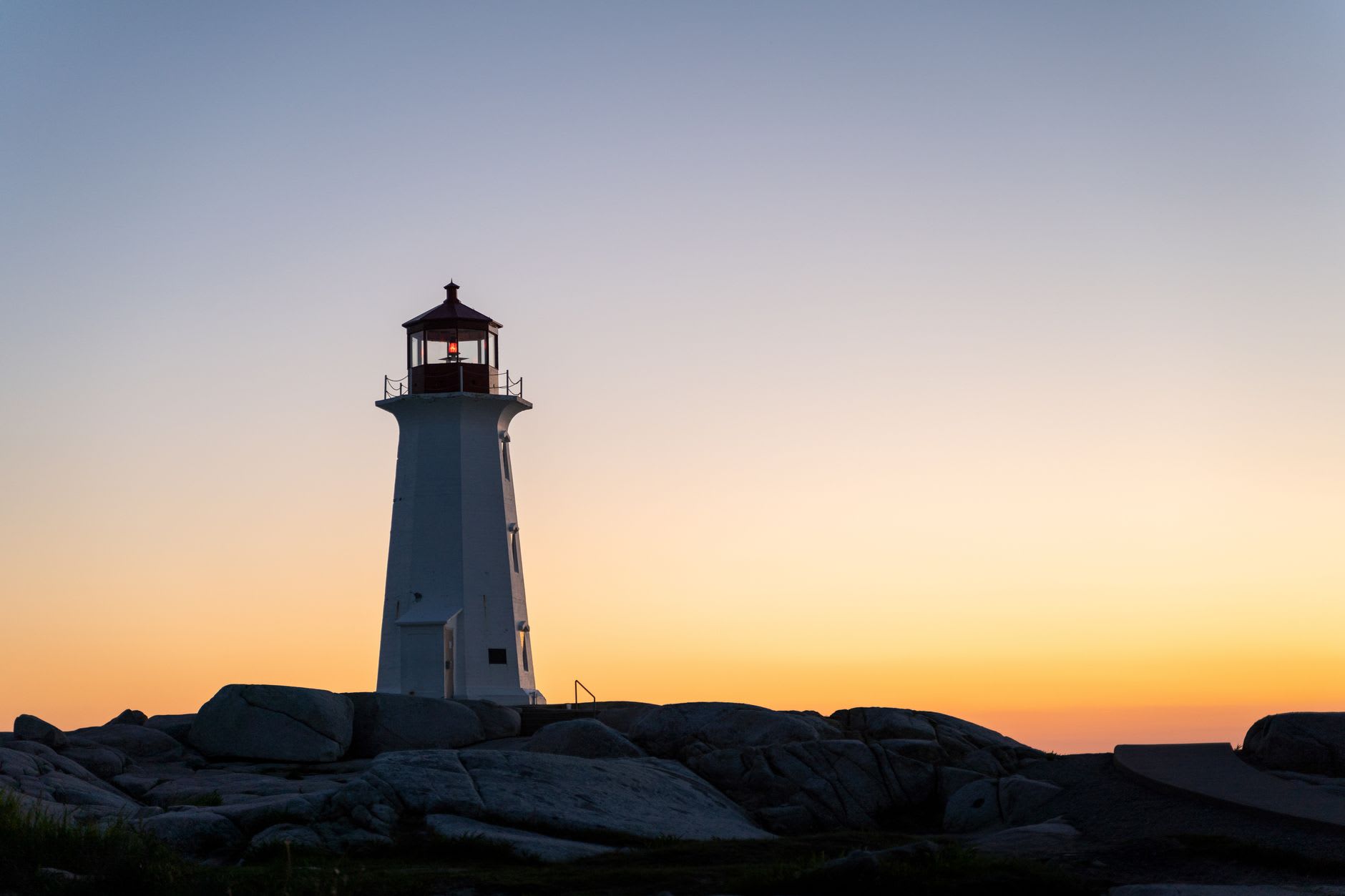 Peggy's Cove lighthouse emerging from Atlantic fog at dawn on its shelf of smooth ancient granite