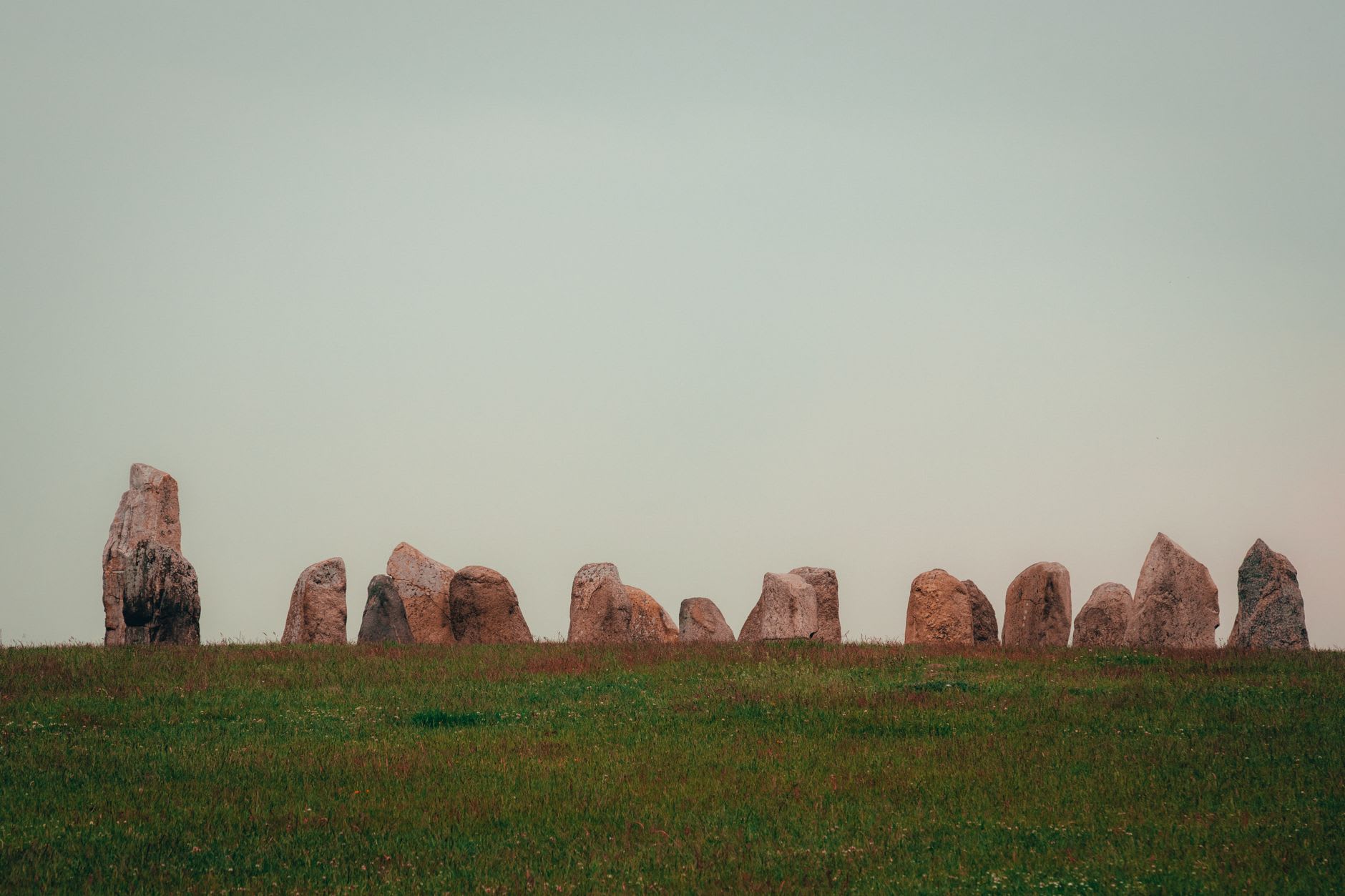 The Ring of Brodgar stones silhouetted against a pale evening sky, the waters of Loch of Harray behind them
