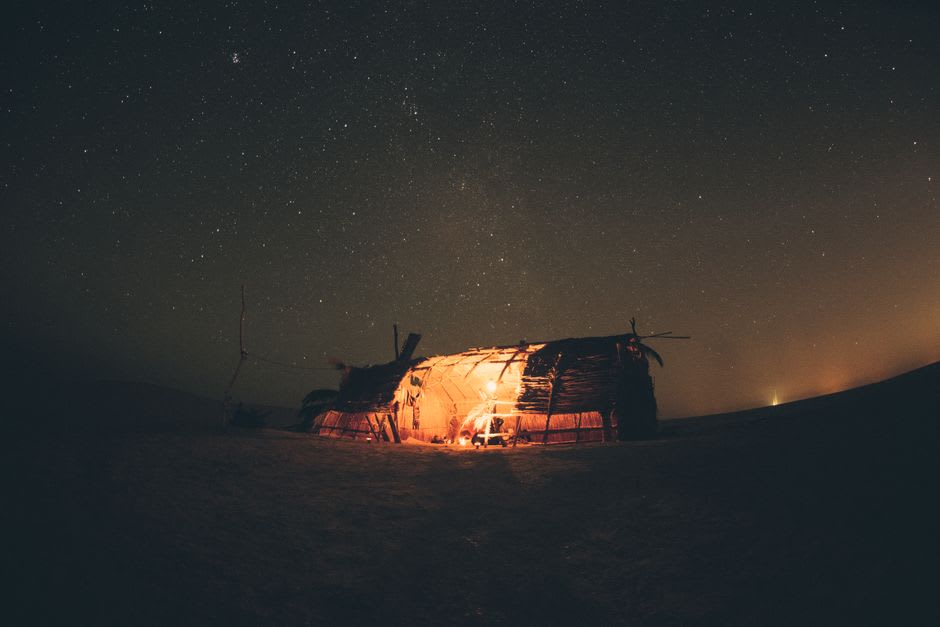 A campsite in a desert swale at night, tents lit softly under an intensely star-filled sky