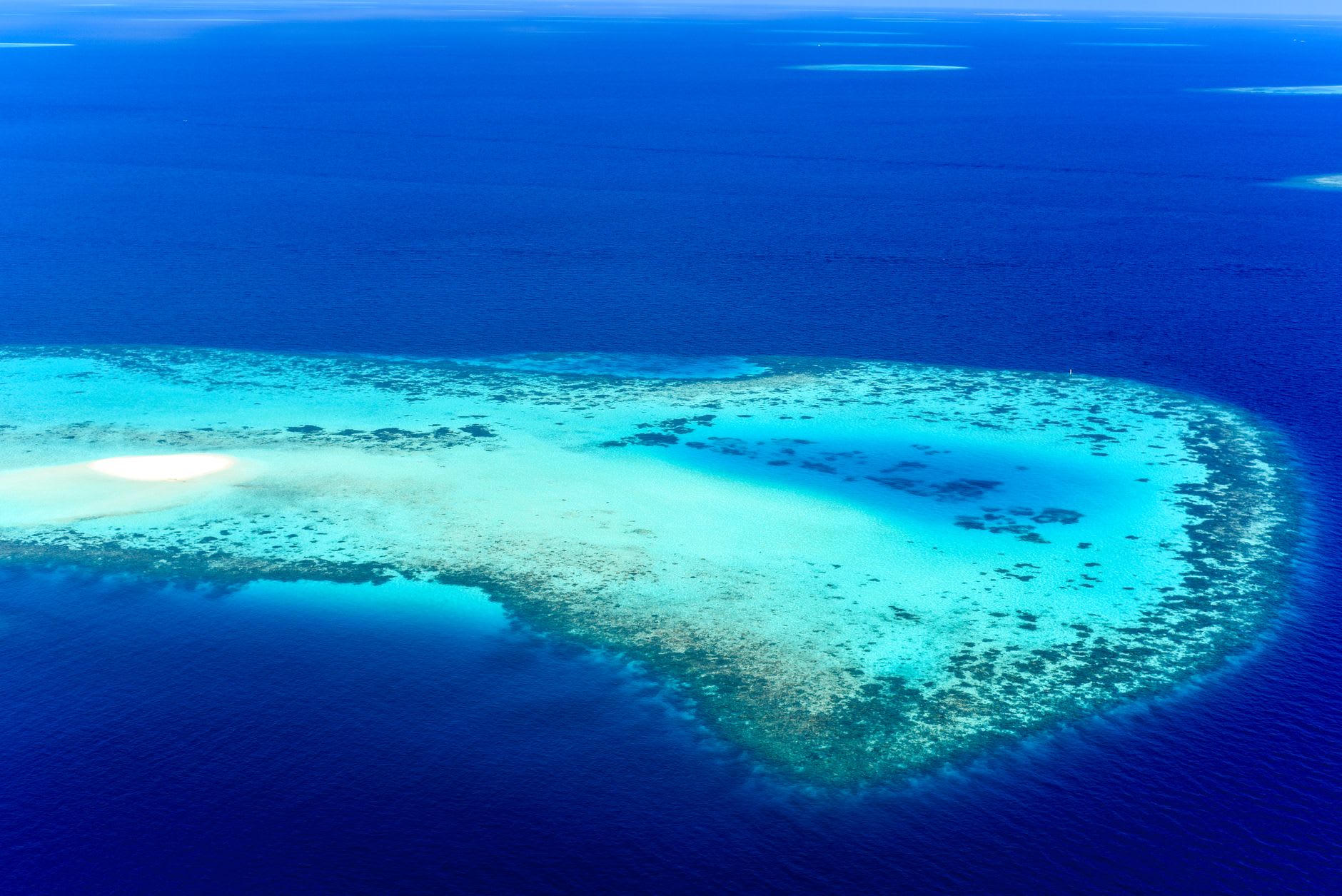 Small fishing boat anchored in the crystal-clear turquoise waters inside Kayangel Atoll, white sand visible beneath the hull