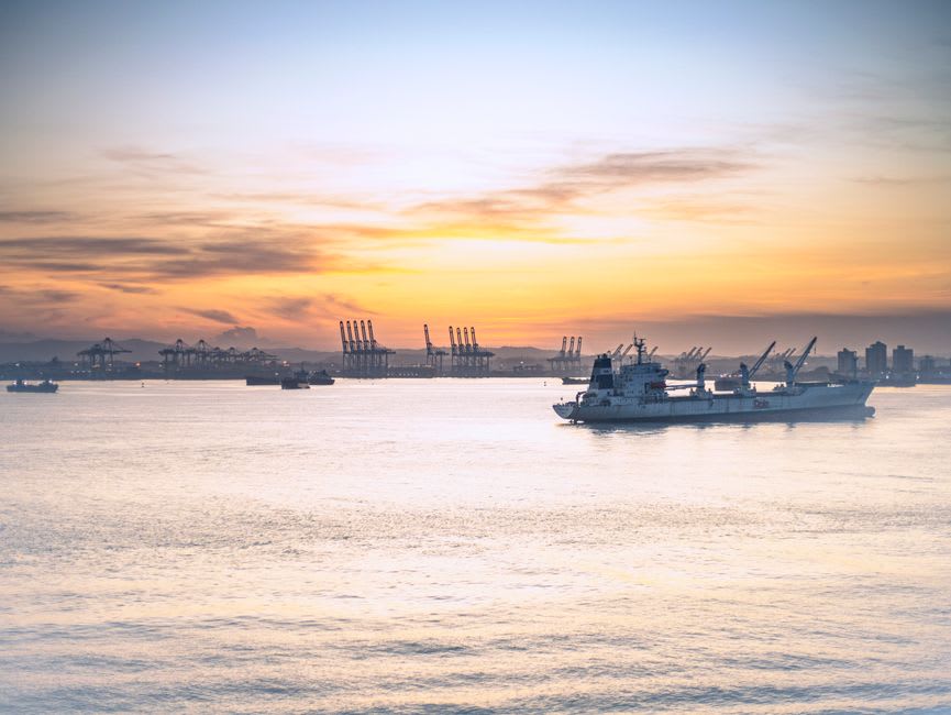 A cargo ship moving through Gatun Lake's open water past a forested island, with a small fishing boat in the foreground