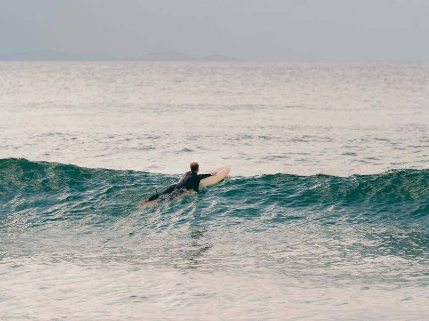 A surfer paddling out through gentle waves at Playa Venao's long horseshoe-shaped bay