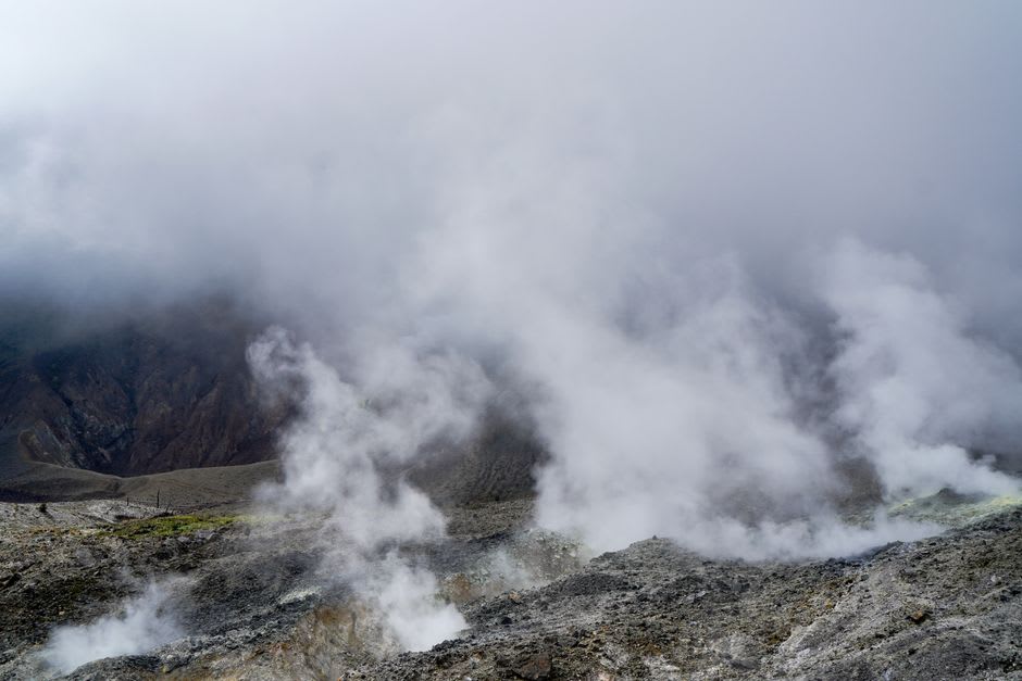 De la vapeur s'élevant d'une fumerolle sur les pentes inférieures du volcan de l'île Karkar, une dense forêt tropicale entourant la roche exposée