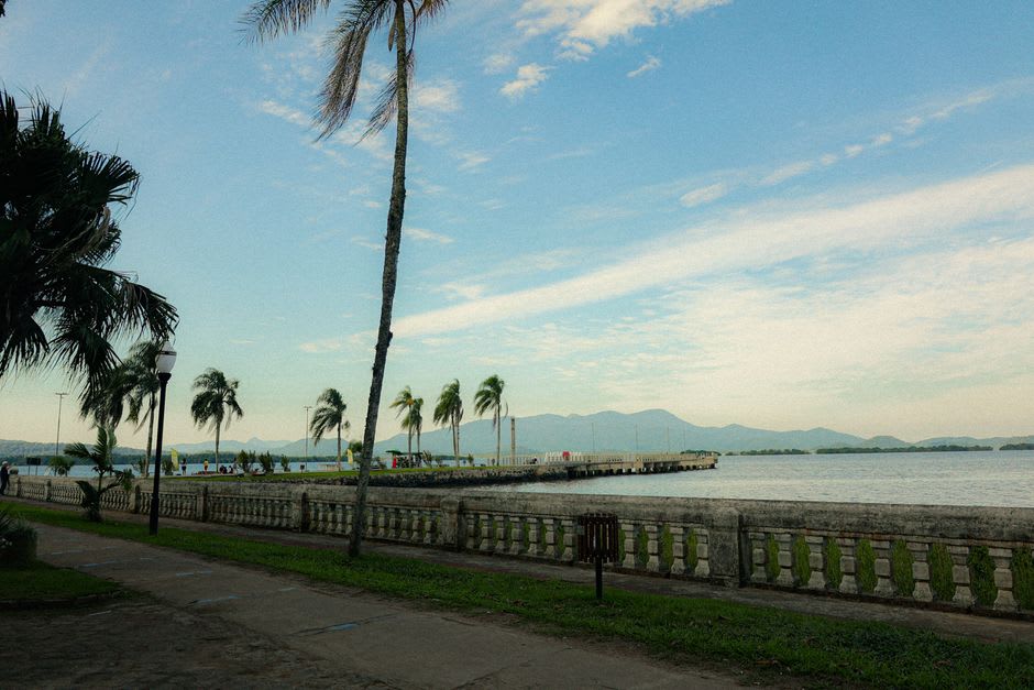 El paseo marítimo junto a la laguna de Madang a la hora dorada, árboles de lluvia dando sombra a un camino donde los lugareños caminan junto a agua en calma y cristalina