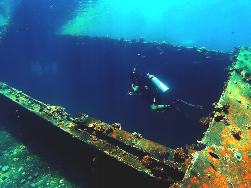Un pecio de la Segunda Guerra Mundial cubierto de coral frente a Madang, bancos de peces pequeños moviéndose por el casco oxidado en aguas azules cristalinas