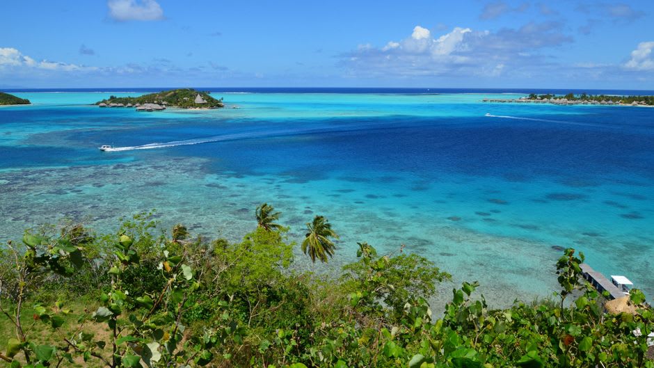 A traditional wooden boat crossing a shallow lagoon near Lorengau on Manus Island, forested islets scattered across clear turquoise water