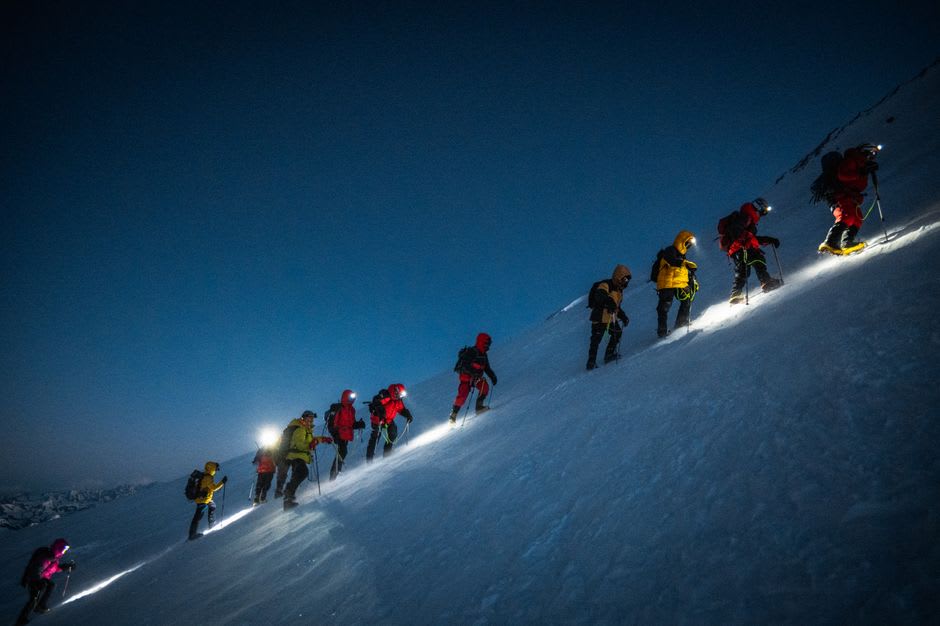 Excursionistas en el ascenso final por pedregal hacia la cresta cumbre del Monte Wilhelm justo antes del amanecer, linternas frontales cortando la oscuridad previa al amanecer