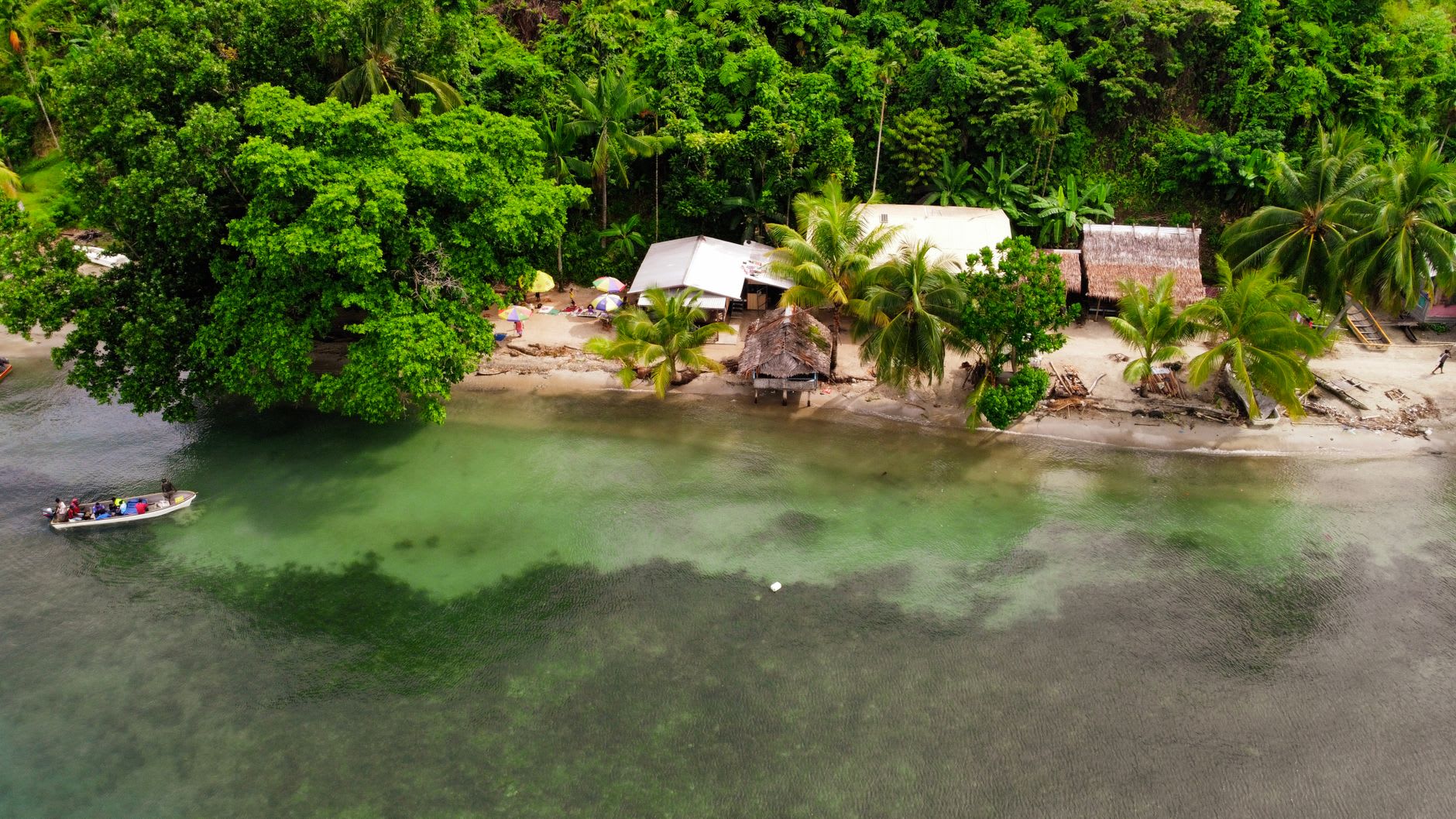 The turquoise lagoon at Kiriwina in the Trobriand Islands, a dugout canoe passing over a shallow coral garden in the afternoon light