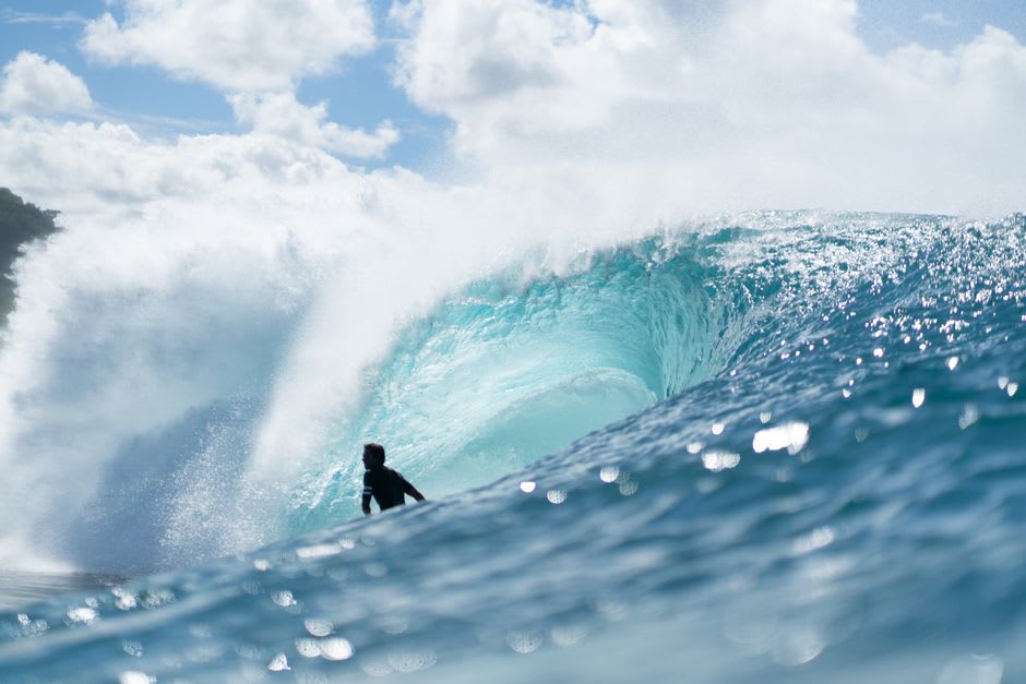 A surfer riding a long point break wave near Vanimo, dense green coastline curving away toward the horizon
