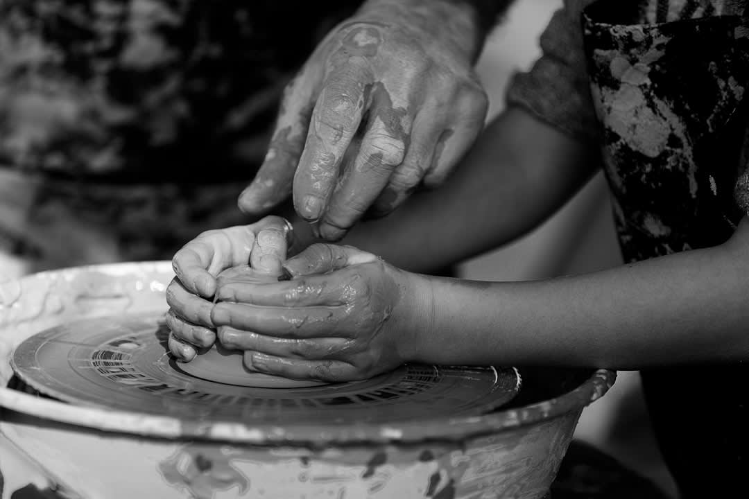 Un primer plano de las manos de una artesana paraguaya pintando detalles delicados en una pequeña figurita de arcilla en un taller de Itá
