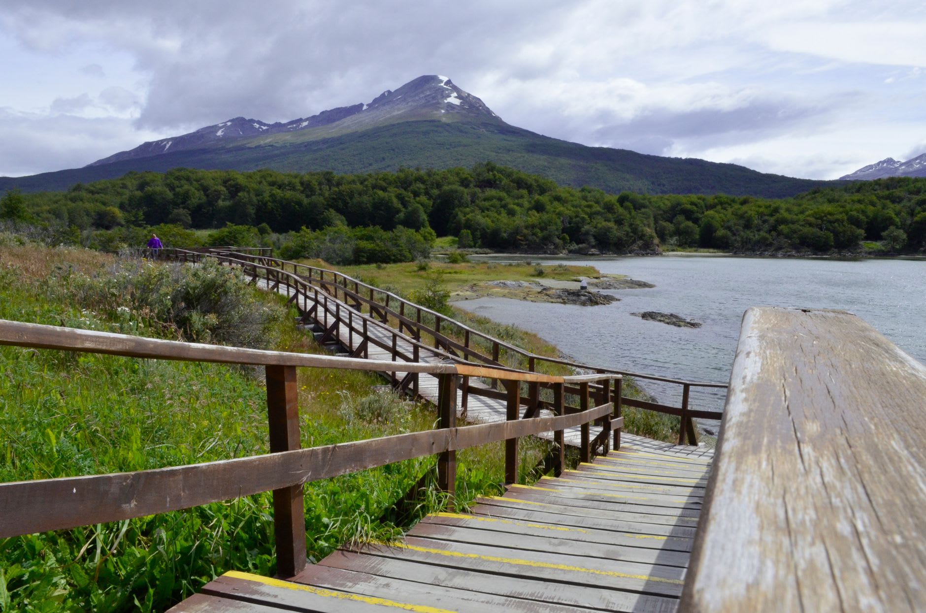 The lighthouse at the Strait of Magellan crossing point, red and white against grey water, beech forest rising behind