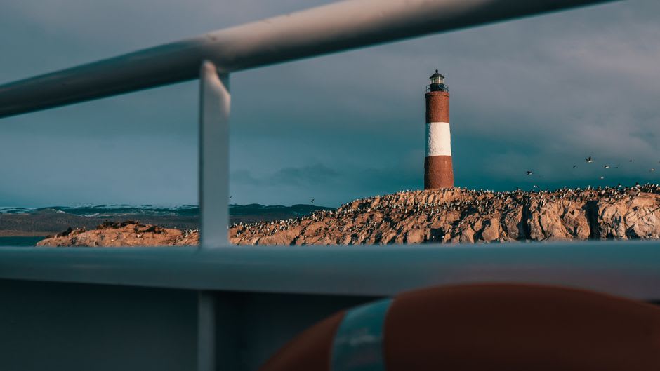 El faro Les Éclaireurs elevándose sobre una pequeña isla rocosa en el canal Beagle, con lobos marinos en las rocas de alrededor
