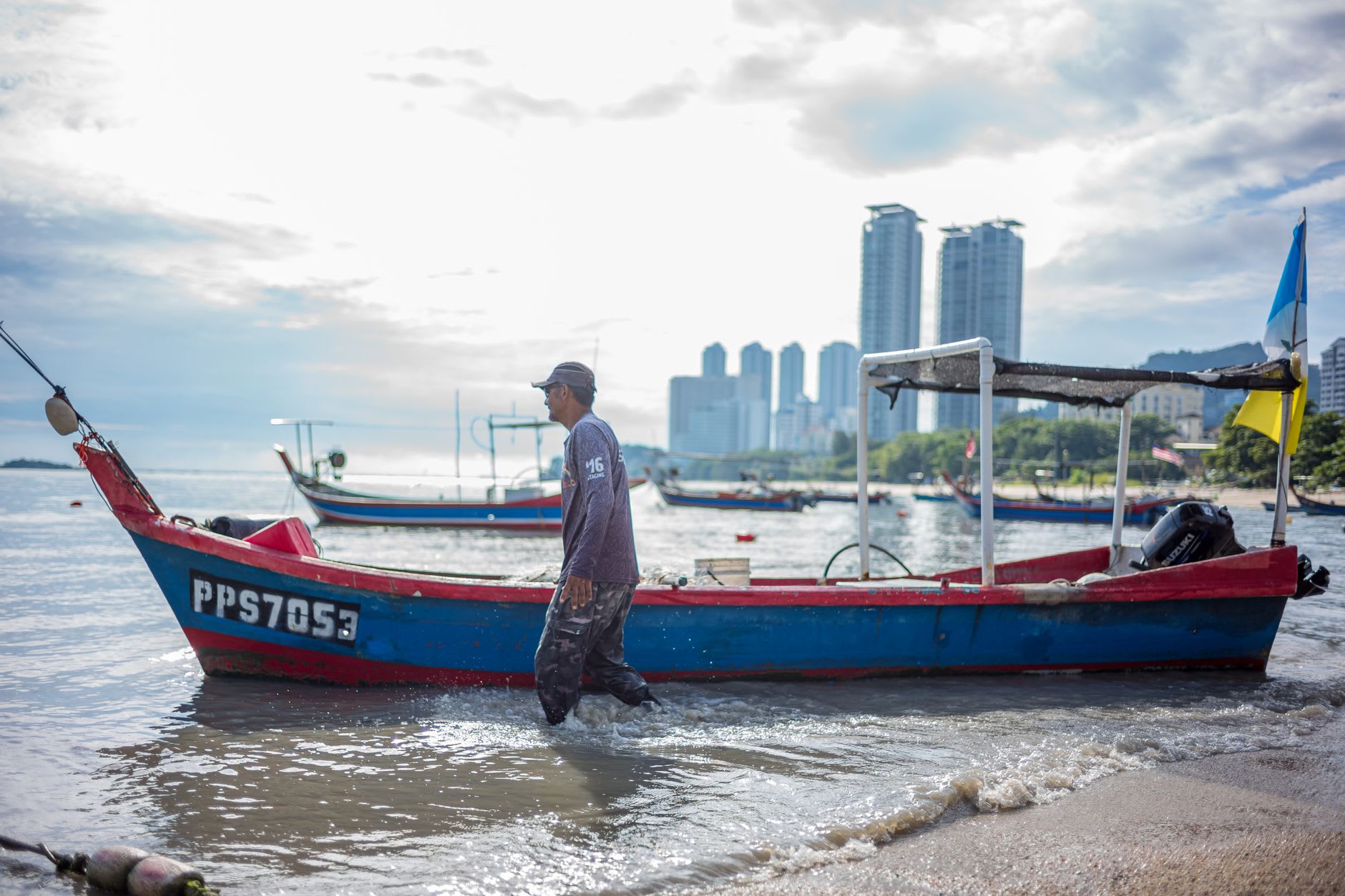 The outer end of a clan jetty with traditional wooden fishing boats moored alongside, the Straits of Malacca beyond
