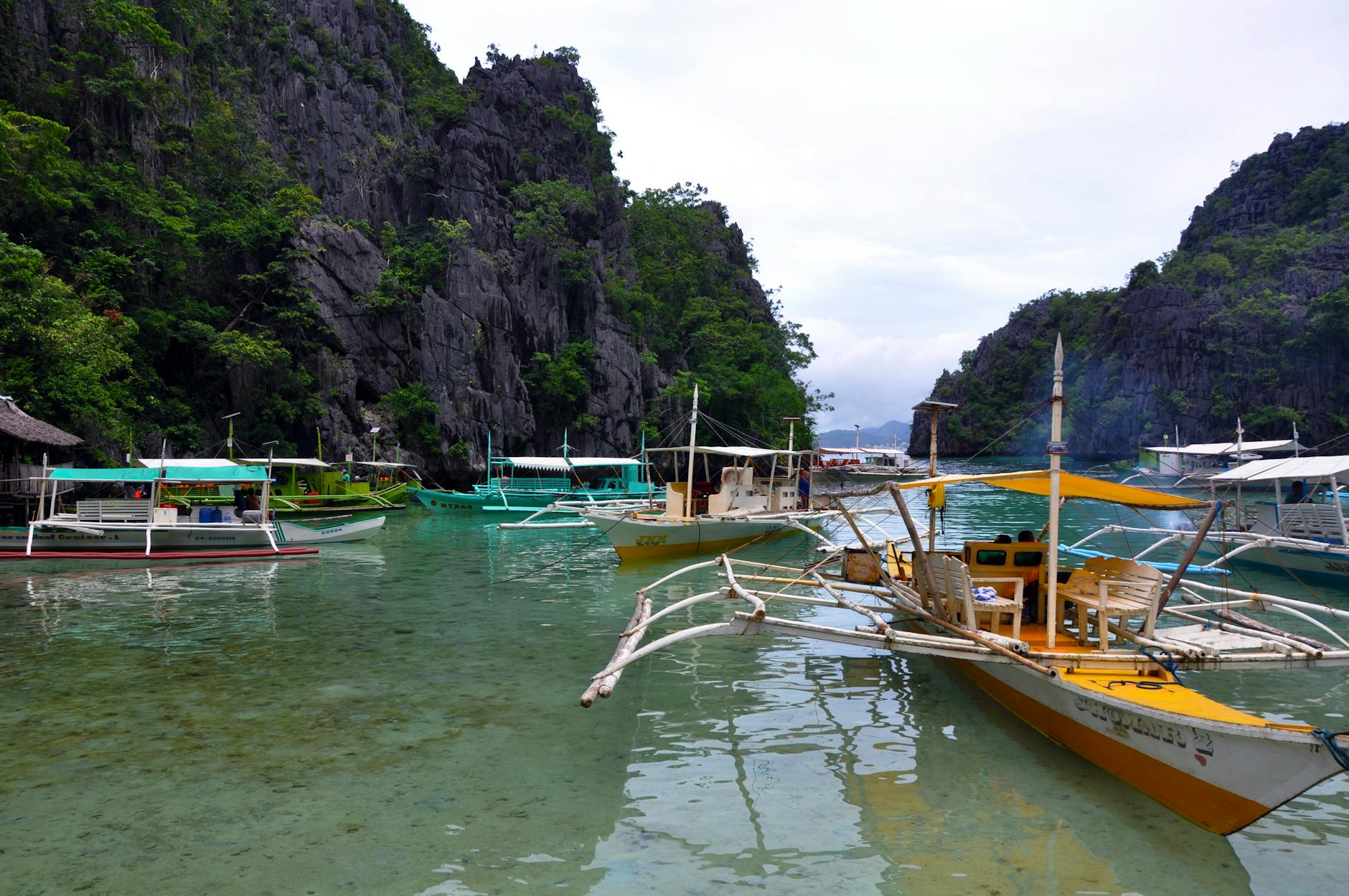 Traditional Filipino outrigger boat floating on crystal-clear turquoise water near limestone cliffs