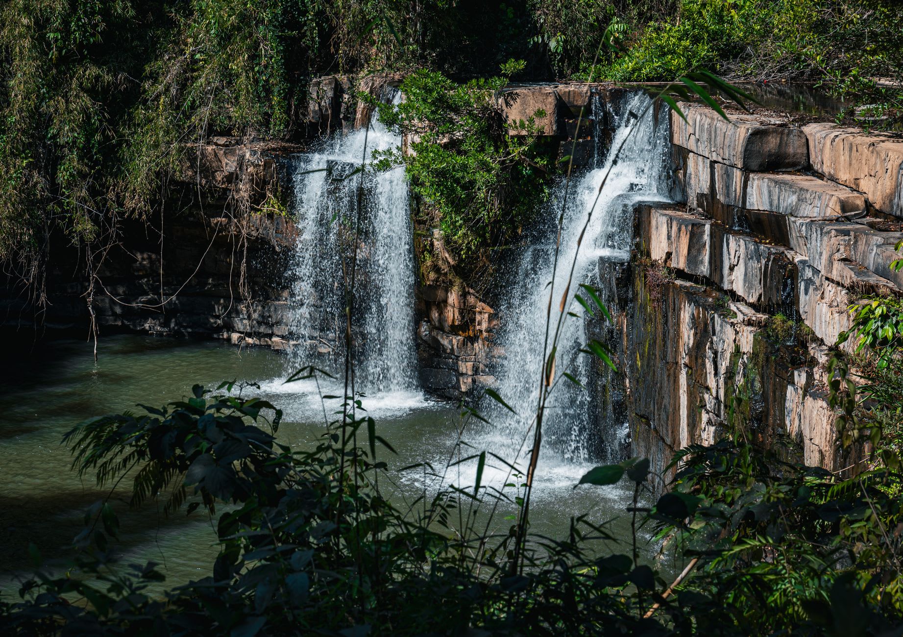 La poza de zambullida de Suoi Tranh desde arriba, la cascada cayendo sobre granito hacia agua tan transparente que el fondo es visible