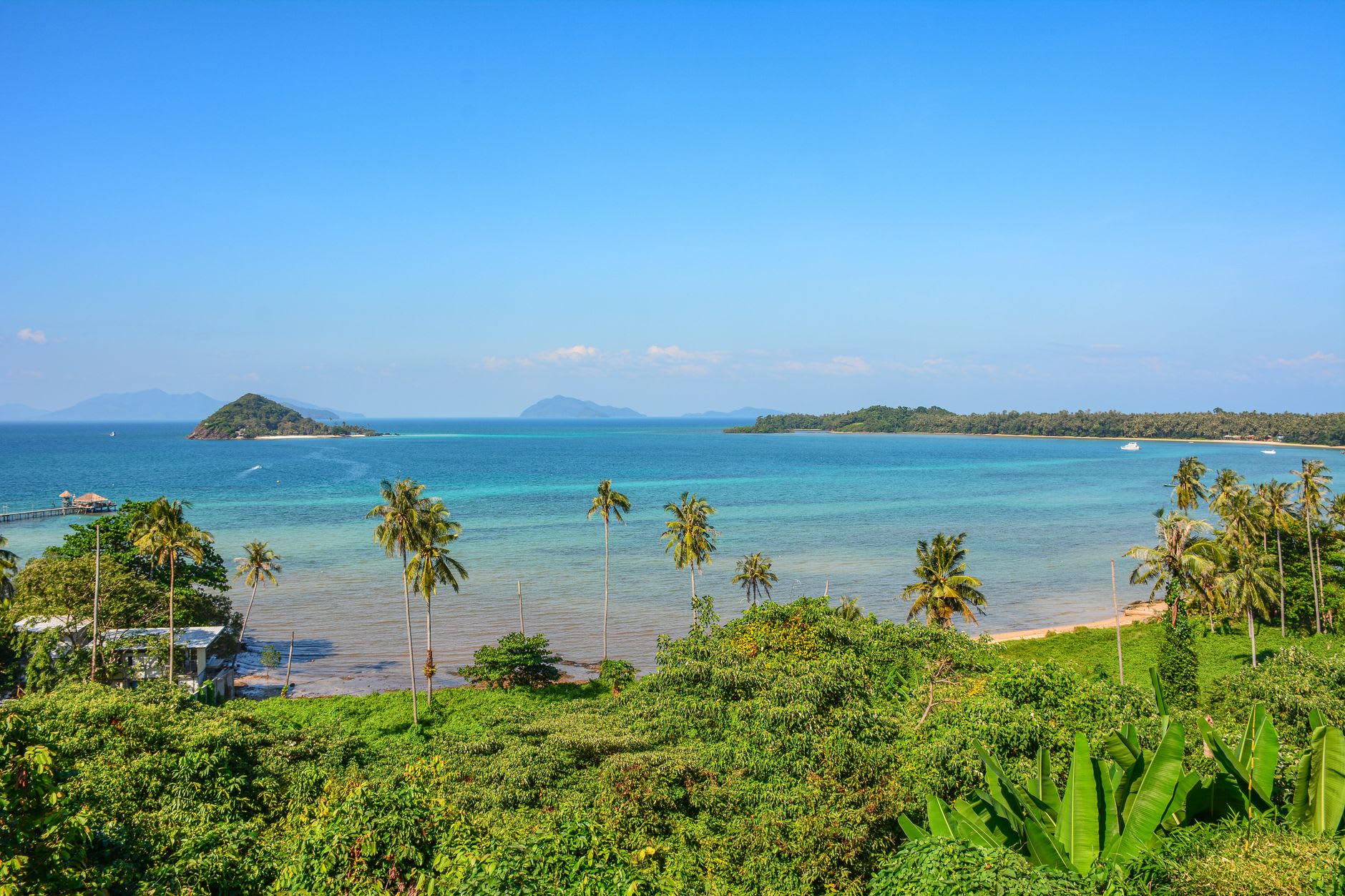 A simple guesthouse garden on Koh Yao Noi, hammocks between palms and limestone karsts visible across the water