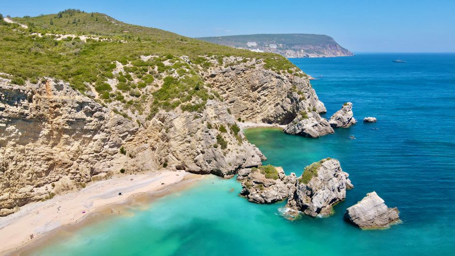 Clear turquoise water and pebble beach at Praia dos Coelhos below the Arrábida cliffs