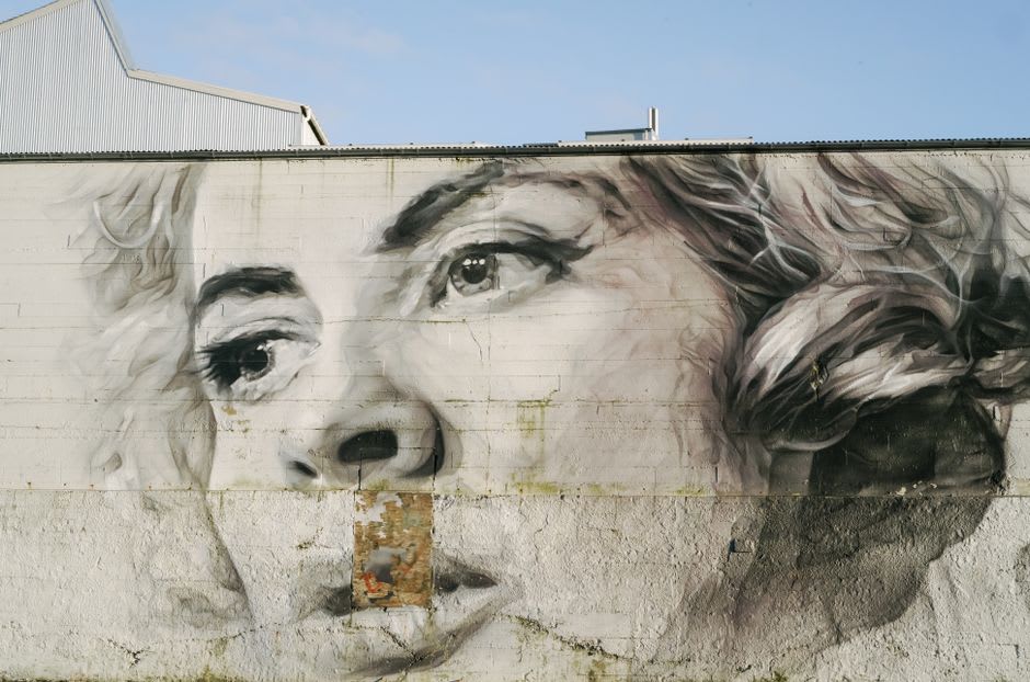 Detail shot of a photorealistic mural face painted across a multi-story former factory building in Covilhã