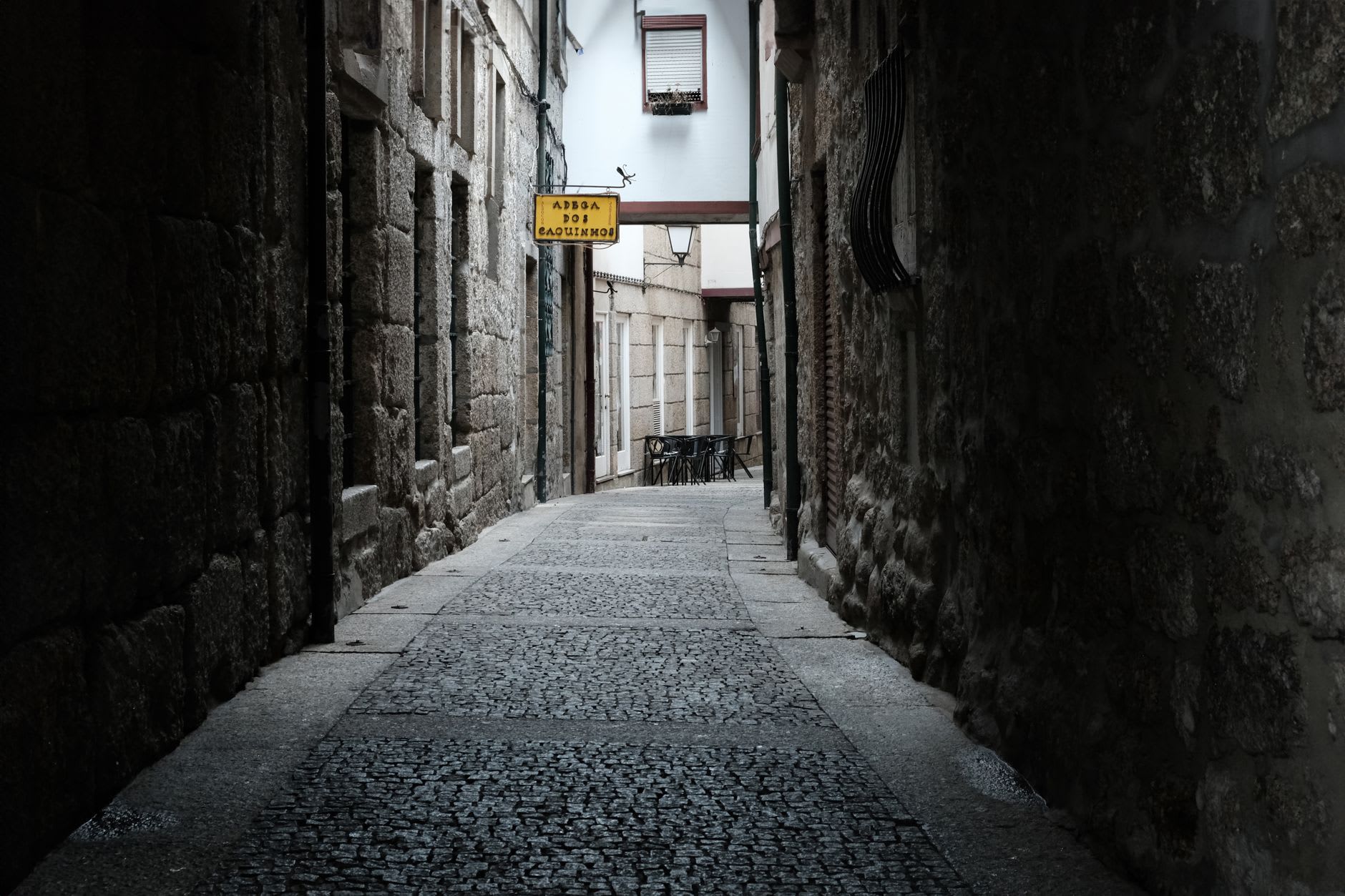 Narrow cobblestone street winding through the medieval old town of Guimarães, flanked by granite buildings with wooden balconies
