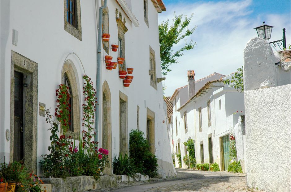 Narrow whitewashed street in Marvão at dusk with wrought-iron balconies and empty cobblestones