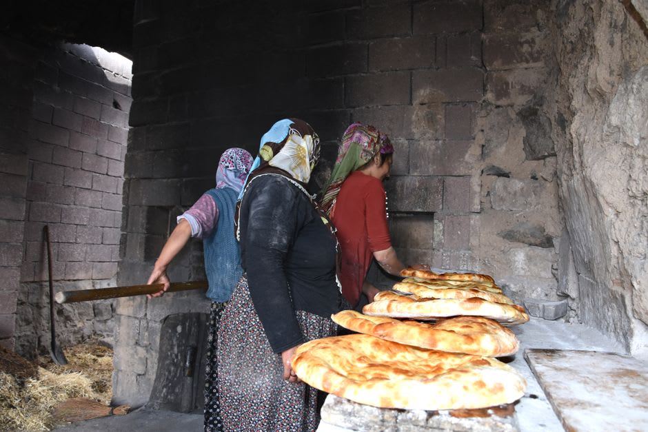 Elderly villager shaping bread dough beside a traditional communal stone oven in a Montesinho village