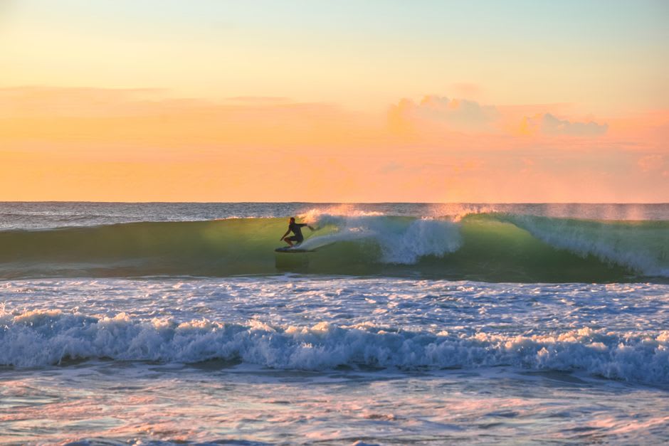 Surfers walking along the shoreline where the river meets the ocean at Praia de Odeceixe during golden hour