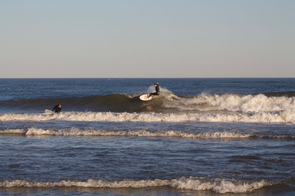 Surfers paddling out into a barreling wave at Praia de Supertubos near Peniche