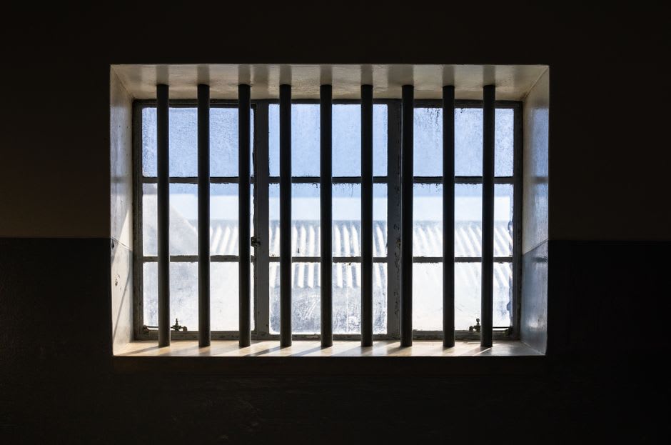 Preserved prison cells inside the Fortaleza de Peniche museum, with harbor light filtering through a small barred window