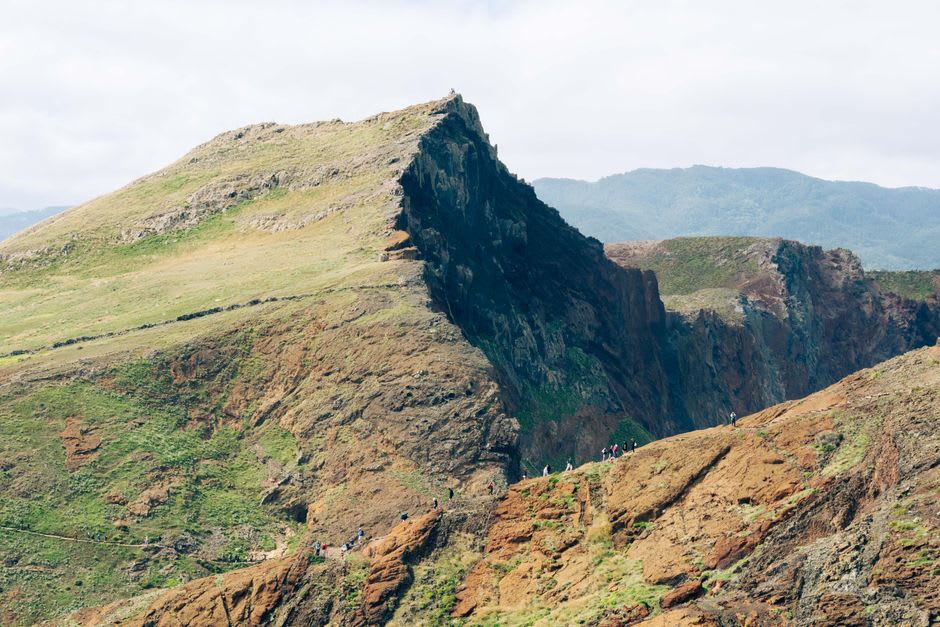 Hikers walking a narrow ridge trail with sheer cliffs on both sides at Ponta de São Lourenço