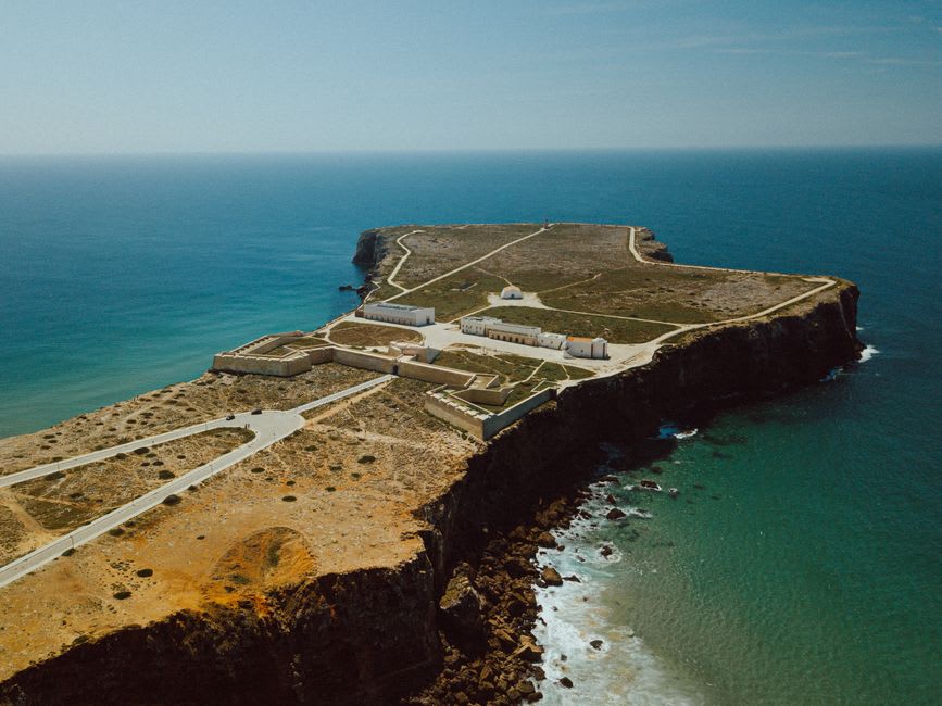 Stone wind compass rose set into the ground at the Sagres fortress with the Atlantic Ocean stretching beyond the cliff edge