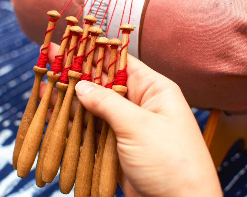 Elderly woman demonstrating traditional bobbin lacemaking with wooden bobbins in Vila do Conde