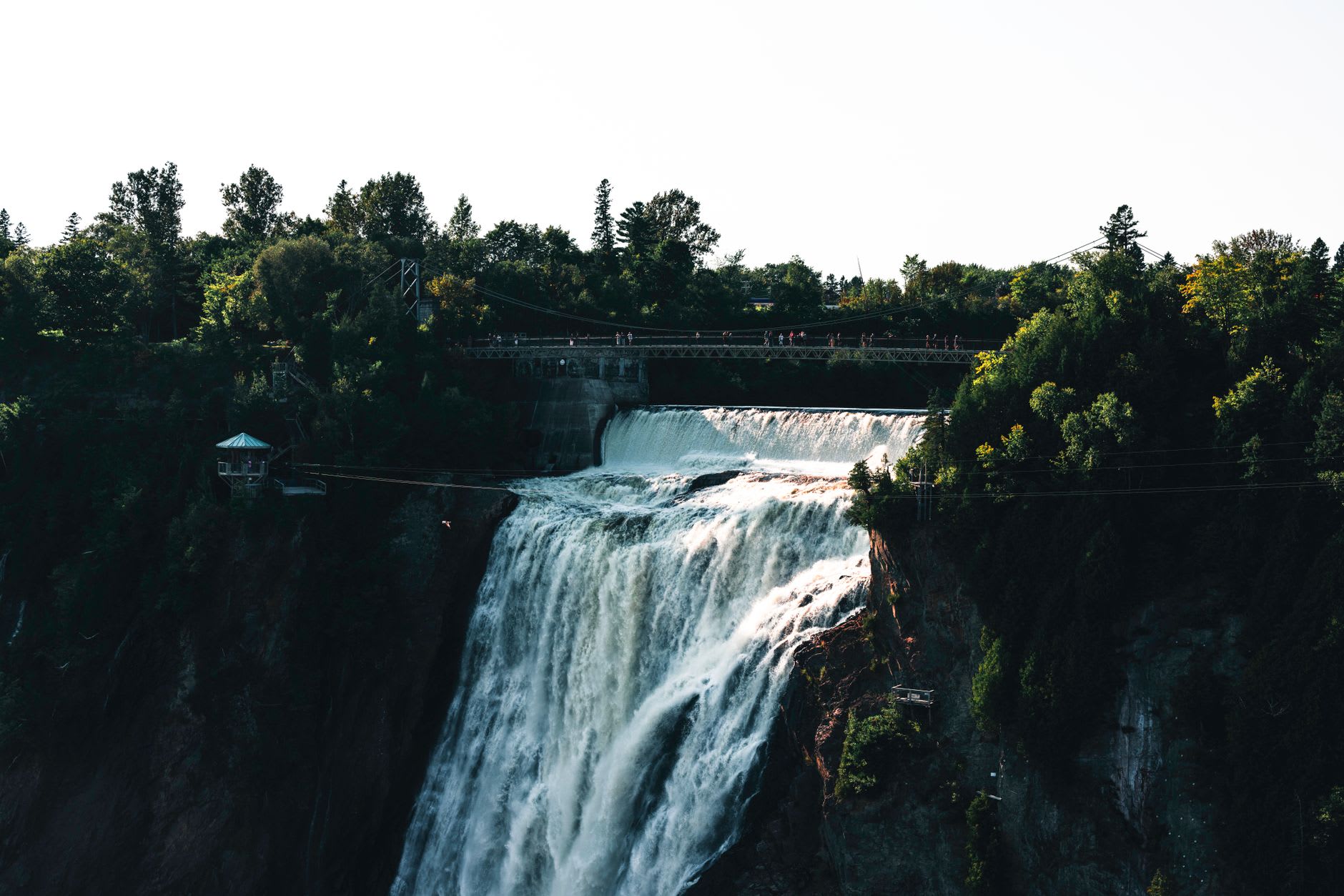 The suspension bridge spanning Montmorency Falls with mist rising from the gorge and the St. Lawrence beyond