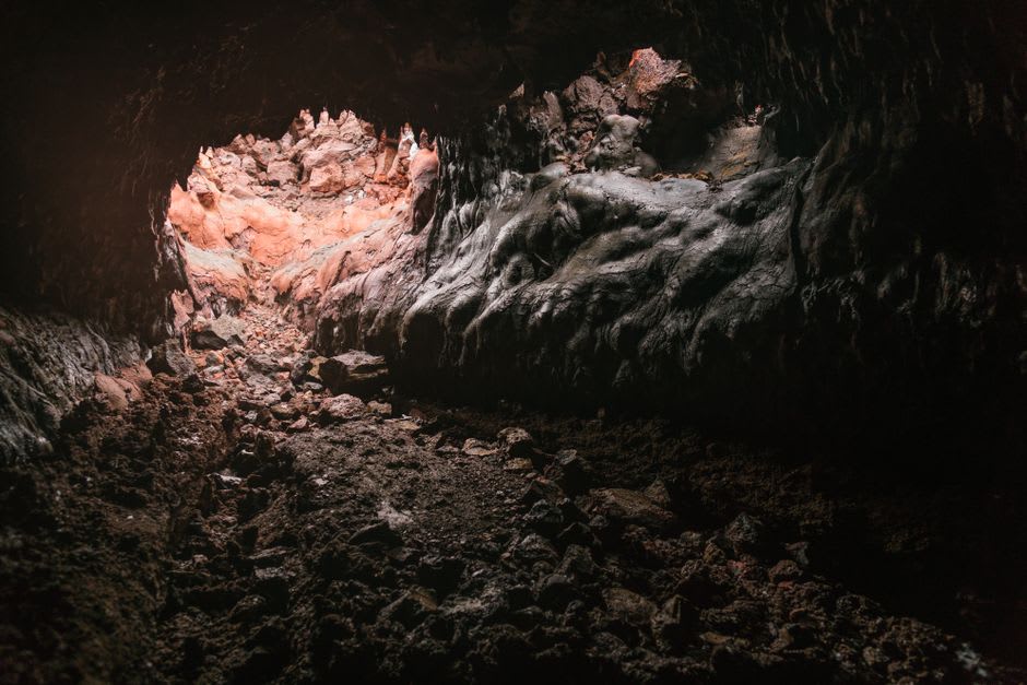 La boca de una cueva de tubo de lava en Undara, luz solar cayendo hacia la oscuridad por una sección colapsada del túnel