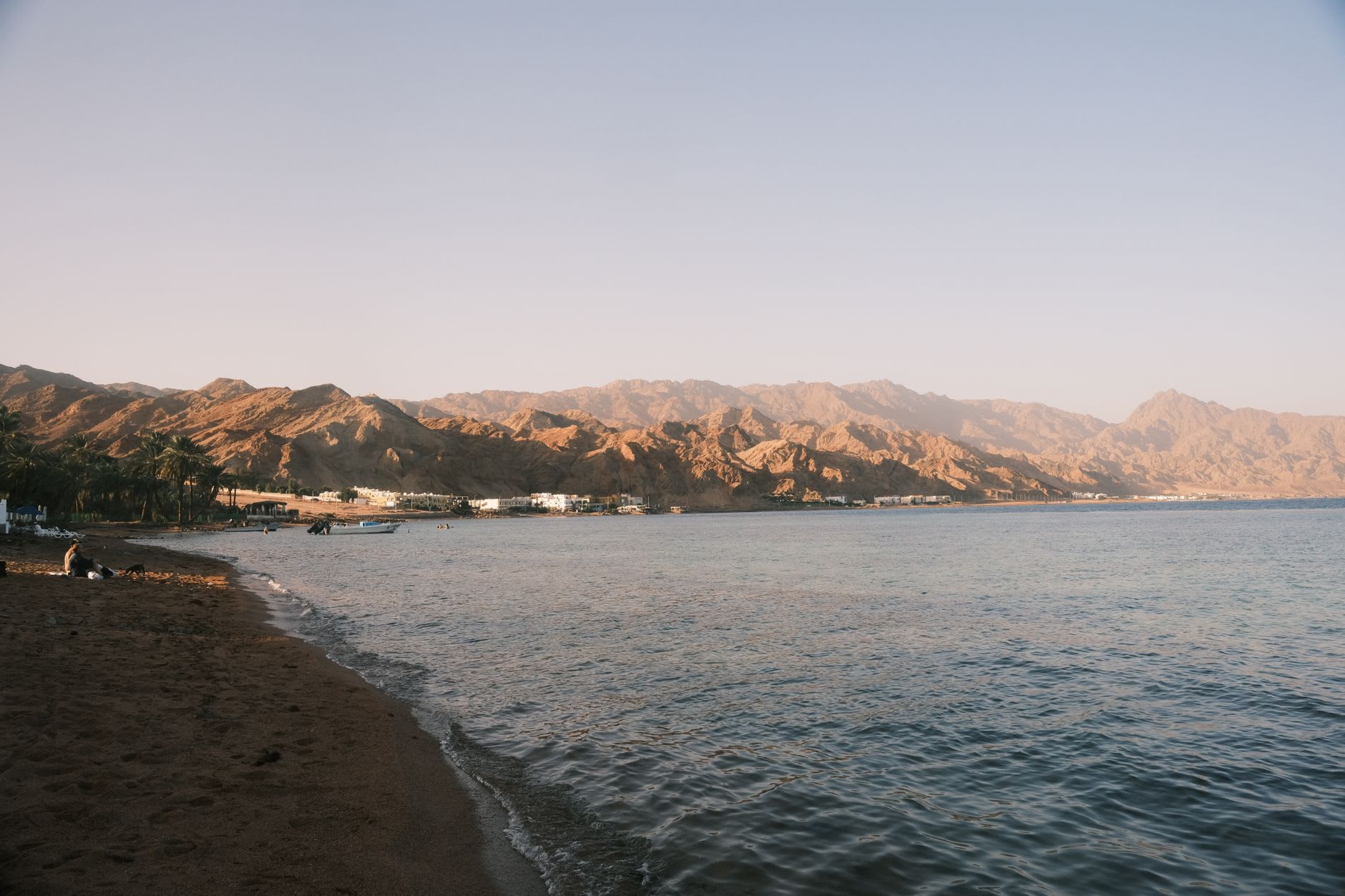 Des bungalows simples en feuilles de palmier sur la plage de Nuweiba au lever du soleil, avec les montagnes de granit rose du Sinaï s'élevant abruptement derrière