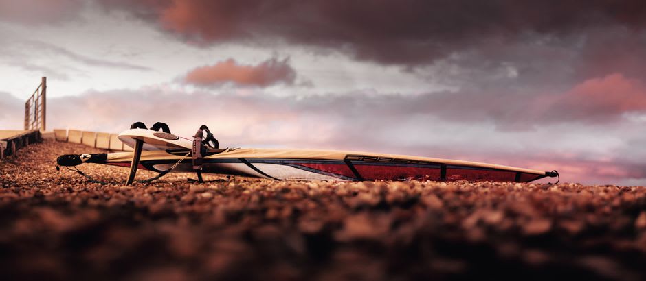 Una fila de tablas de windsurf alineadas en la arena de Safaga con el agua de la bahía llena de crestas blancas al fondo
