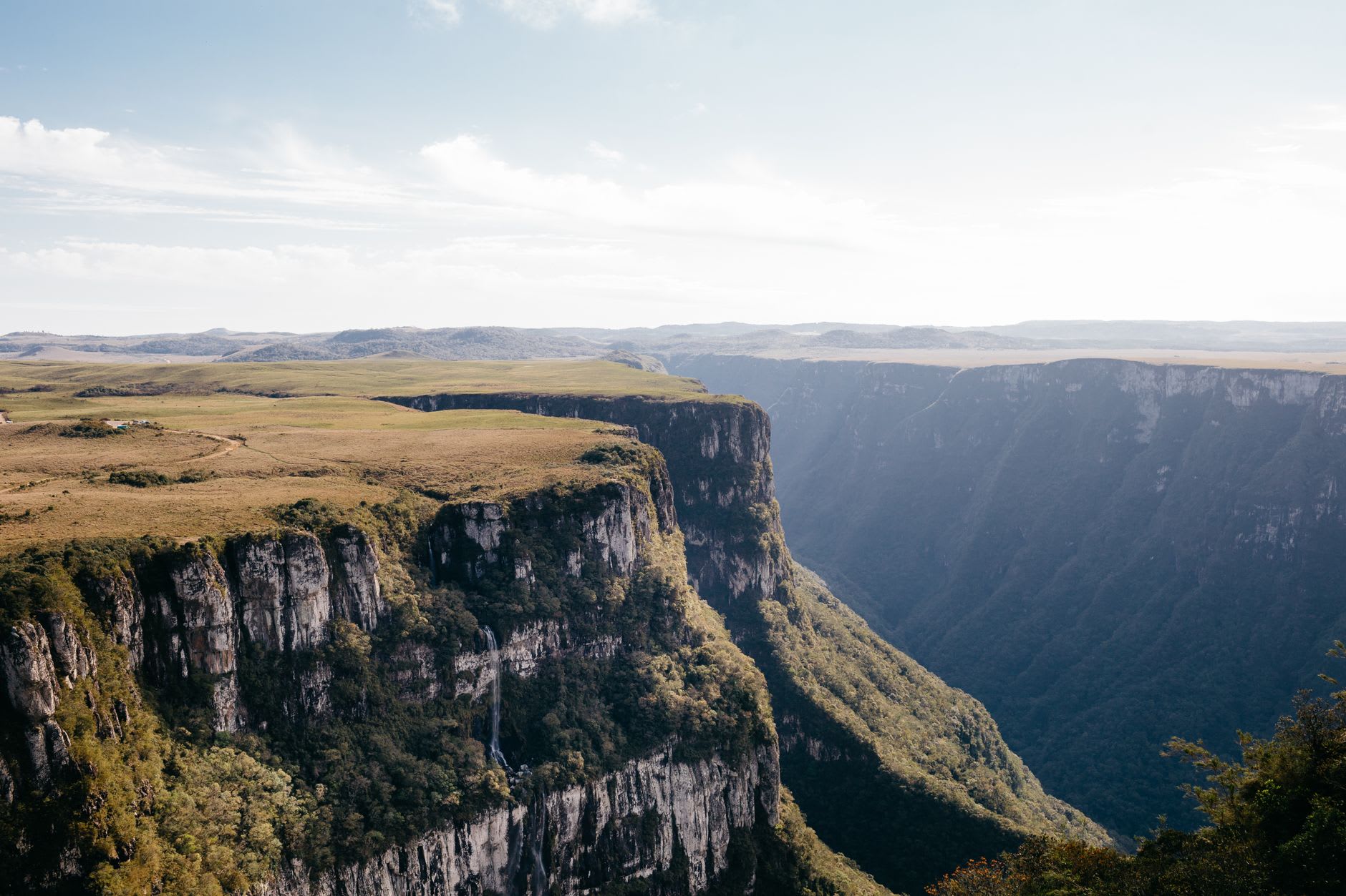 Hikers standing near the Pedra do Segredo rock slab at the cliff edge of Cânion Fortaleza, mist rising from the canyon below