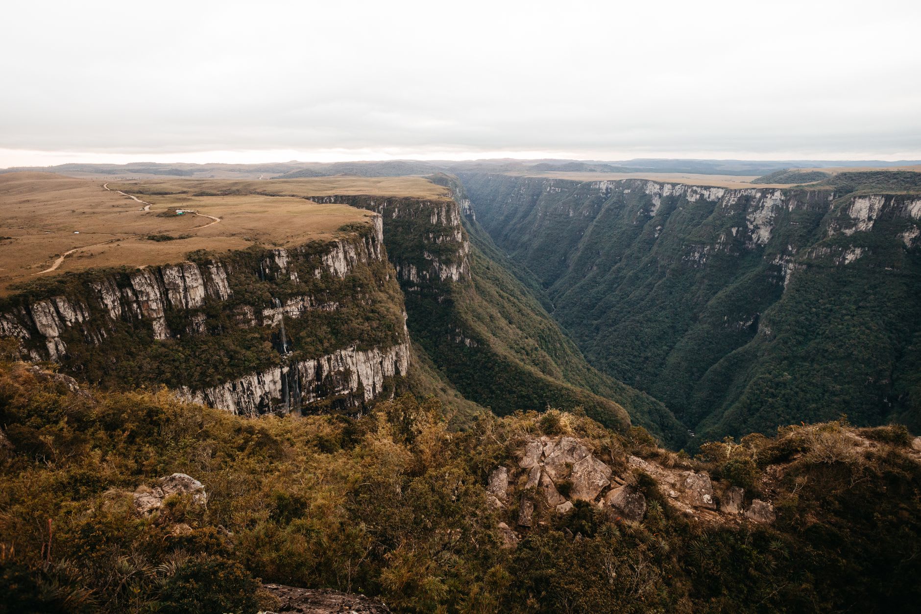 A thin waterfall dropping from the canyon rim at Itaimbezinho, disappearing into the deep shadow of the canyon floor, morning mist rising from below