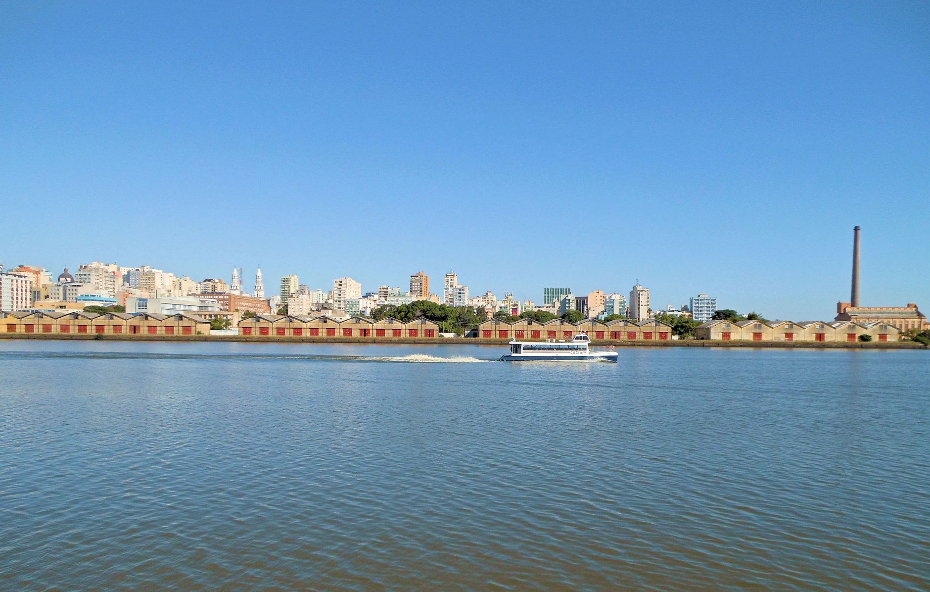 People gathered along the Guaíba waterfront at golden hour, the river glowing orange and violet