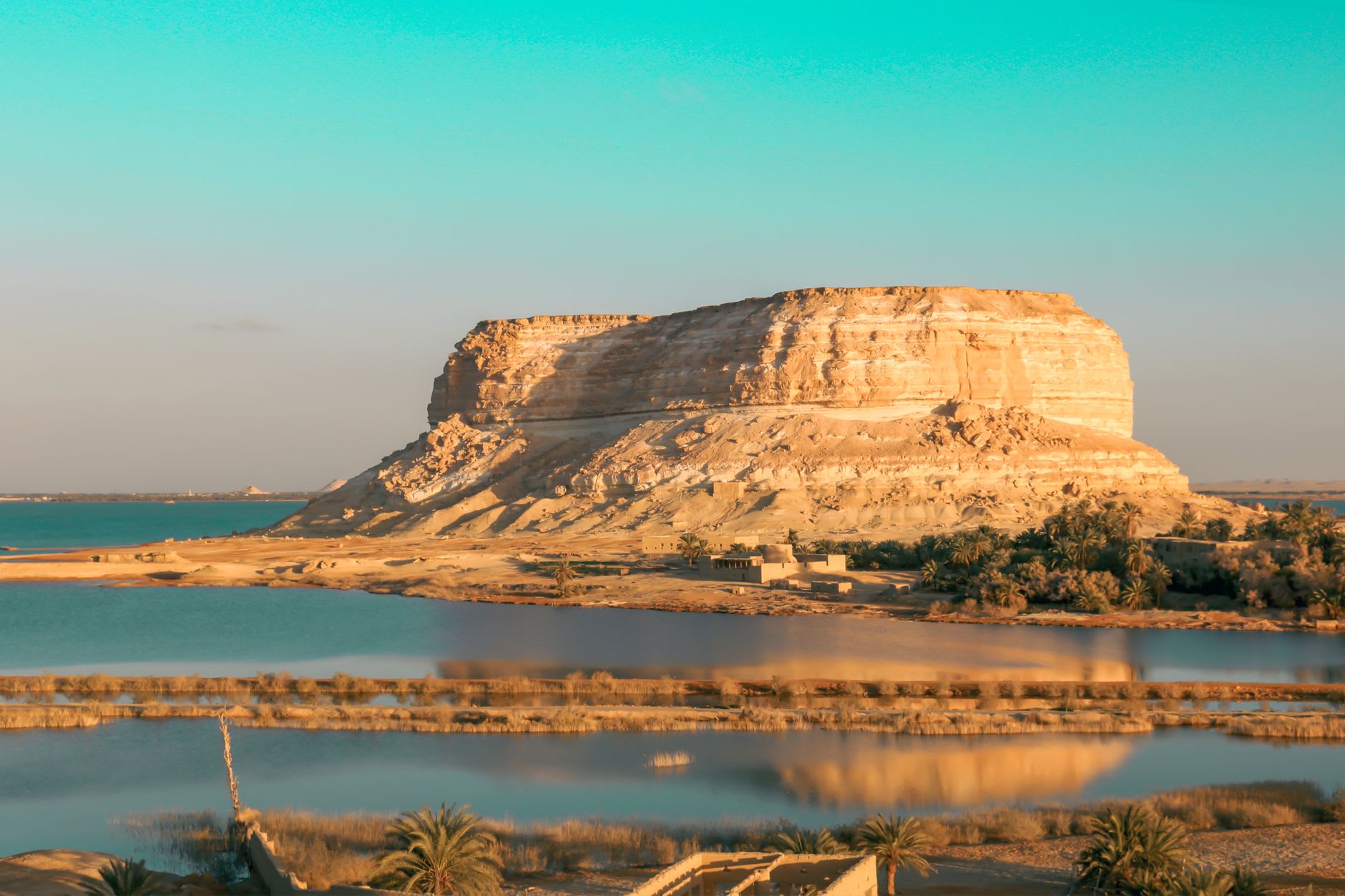 Ein Guba spring — warm clear water in a stone pool surrounded by date palms in the late Siwa afternoon