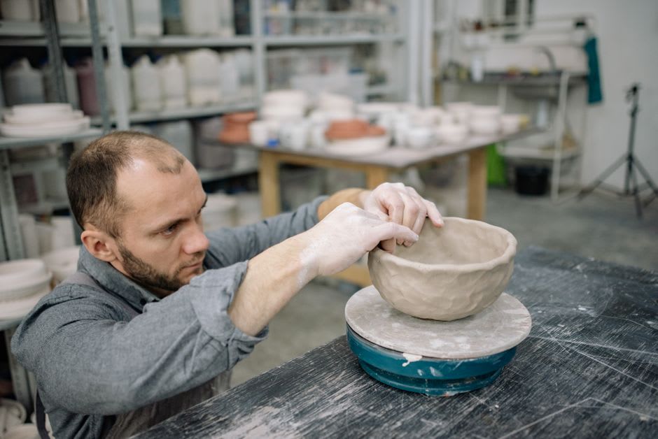 A potter shaping clay by hand on a manual wheel at a workshop in La Fargue, Choiseul