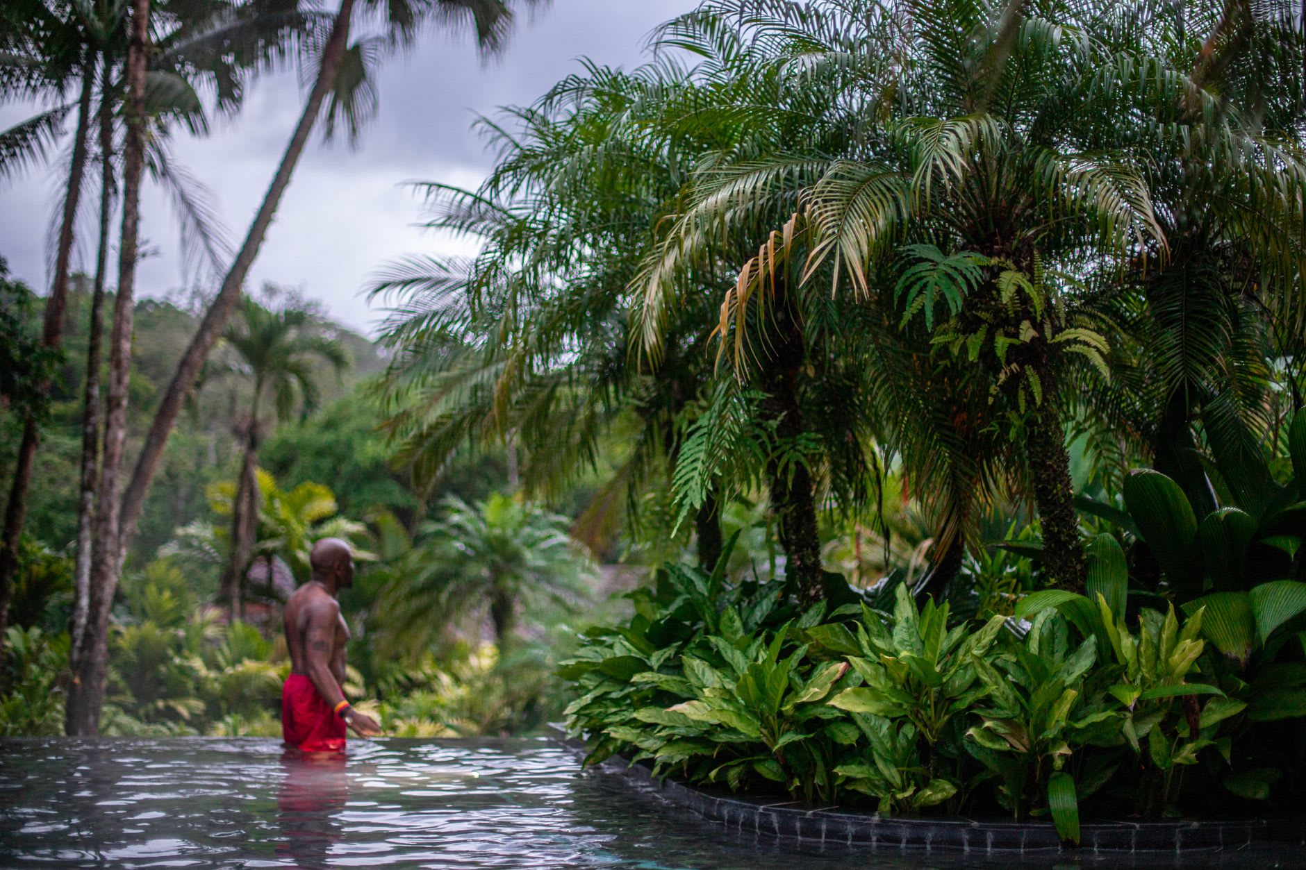 Visitors in the volcanic mud pools below Sulphur Springs, grey mineral mud and steam, palm trees and blue Caribbean sky overhead