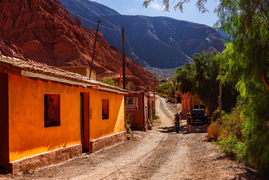 A weathered adobe house in Alfarcito with the canyon's colored rock layers rising behind
