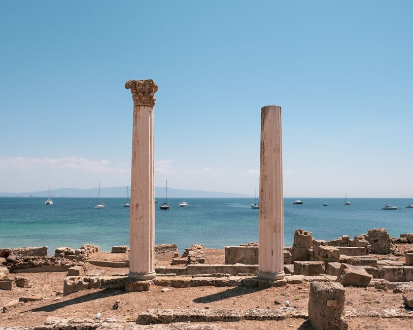 Two restored Corinthian columns standing among the excavated Roman street grid of Tharros with the sea beyond