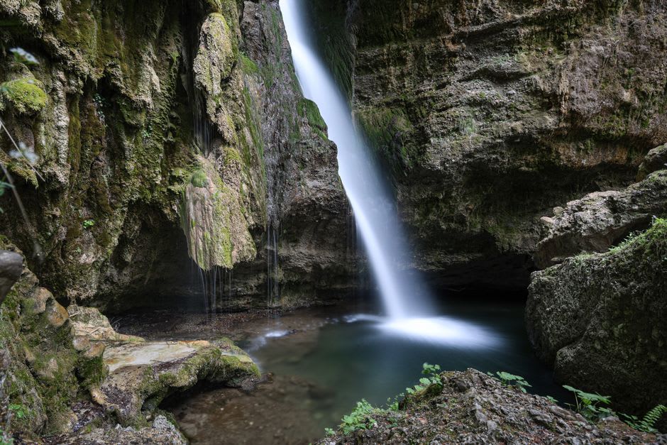 The Šum waterfall crashing into a pool at the end of Vintgar Gorge, surrounded by dense forest