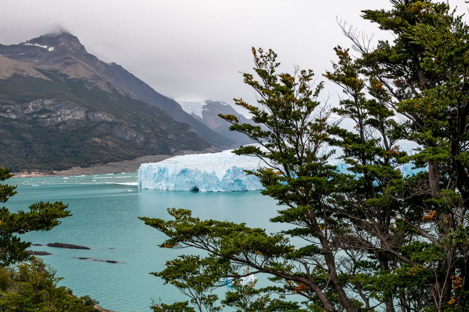 The turquoise glacial lagoon at the base of the hanging glacier waterfalls, ringed by dense green rainforest