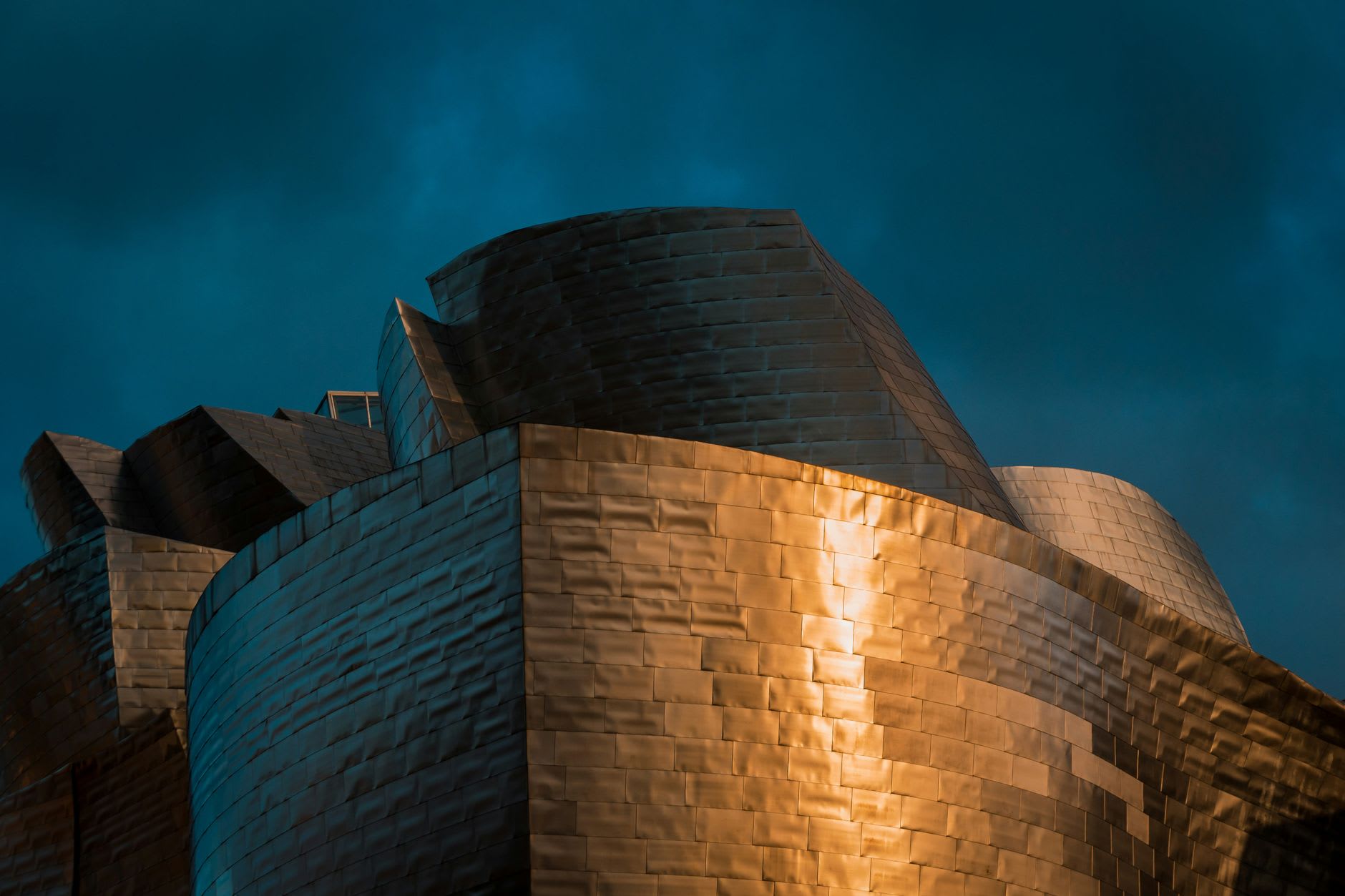 The Guggenheim Bilbao's titanium facade reflecting afternoon light beside the Nervión river