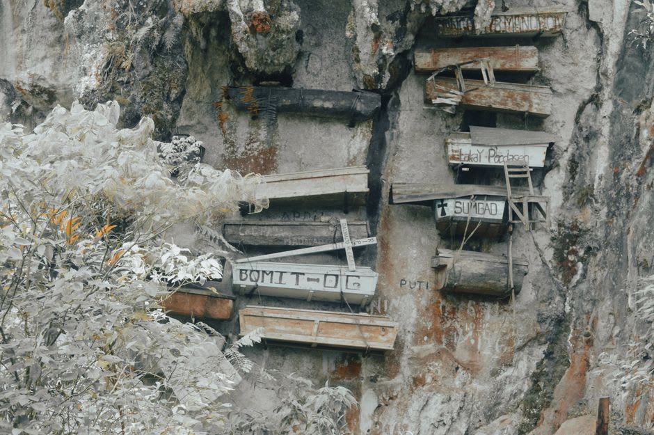 Antiguos ataúdes de madera tallados con motivos animales colgando de una abertura de cueva en el acantilado de Kete Kesu