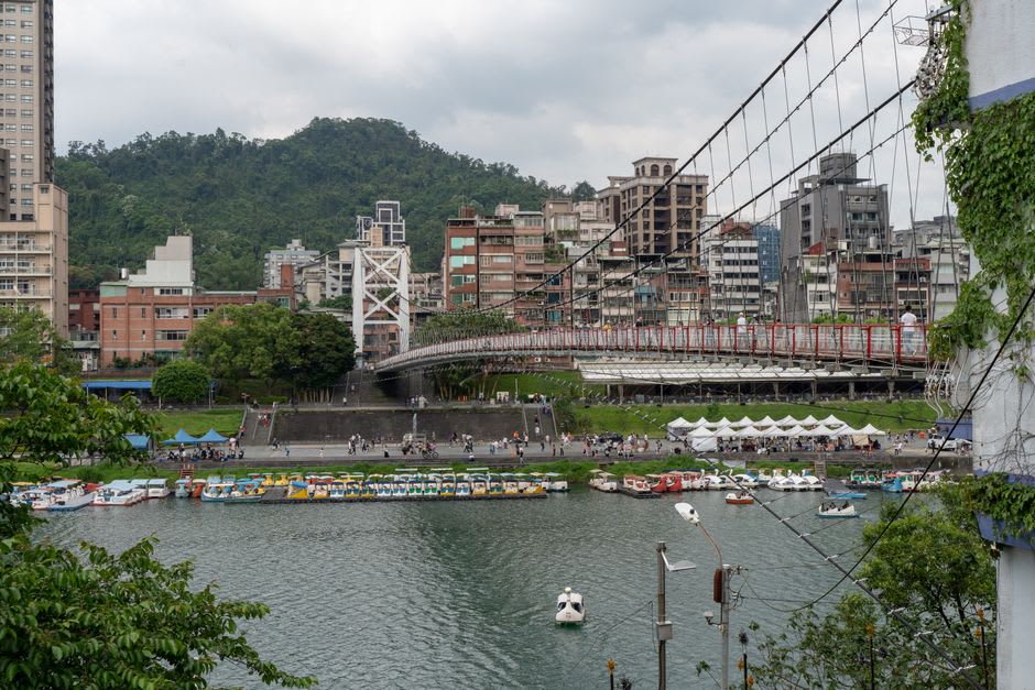 The red suspension bridge over Bitan's jade-green water, dozens of white swan-shaped paddle boats scattered across the surface below