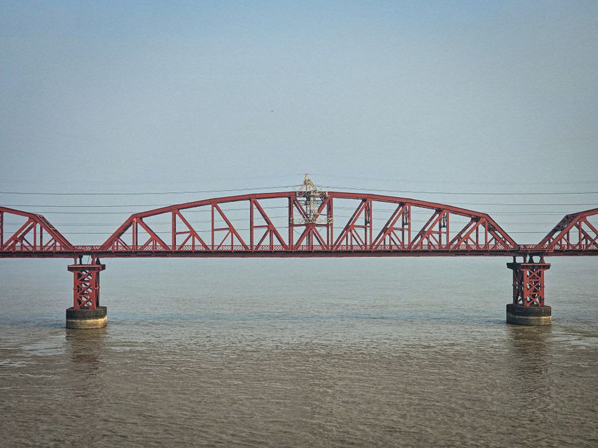The red arched Fulong footbridge spanning the river mouth, with kayakers on the calm water below and the ocean beyond